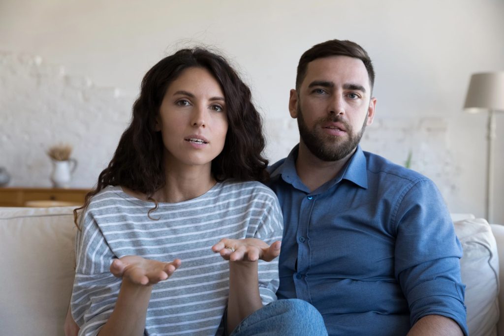 A couple sits together on a couch, appearing engaged in a conversation.