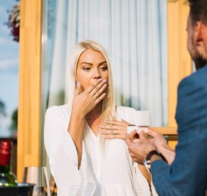 A person is surprised as another presents a ring, suggesting a marriage proposal.