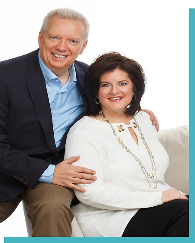 A smiling couple sits together, dressed in business attire.