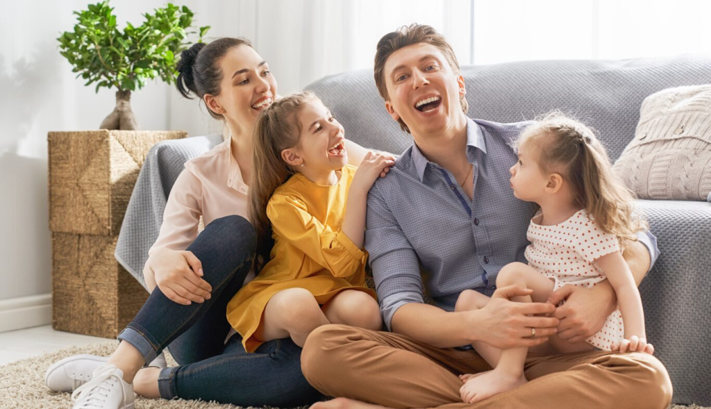 A happy family of four seated together, smiling and laughing in a cozy living room setting.