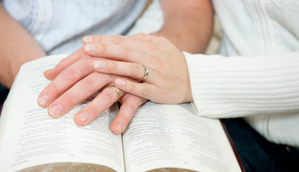 Hands with rings resting on an open book, symbolizing unity or connection.