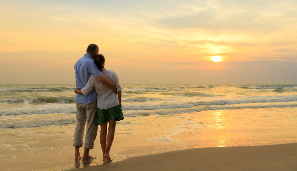 A couple embraces while watching a sunset on a beach, symbolizing a romantic moment.
