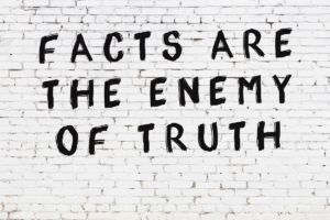 "FACTS ARE THE ENEMY OF TRUTH" is written on a white brick wall.