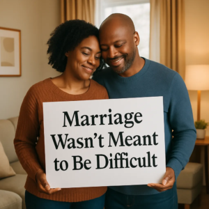 A couple smiles while holding a sign that says, "Marriage Wasn't Meant to Be Difficult."