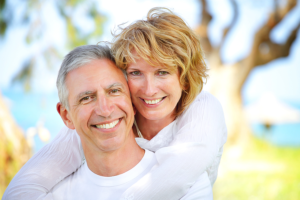 Mature couple outdoors, wearing white shirts, smiling and embracing each other.