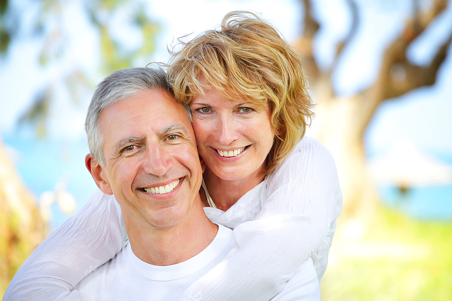 Mature couple outdoors, wearing white shirts, smiling and embracing each other.
