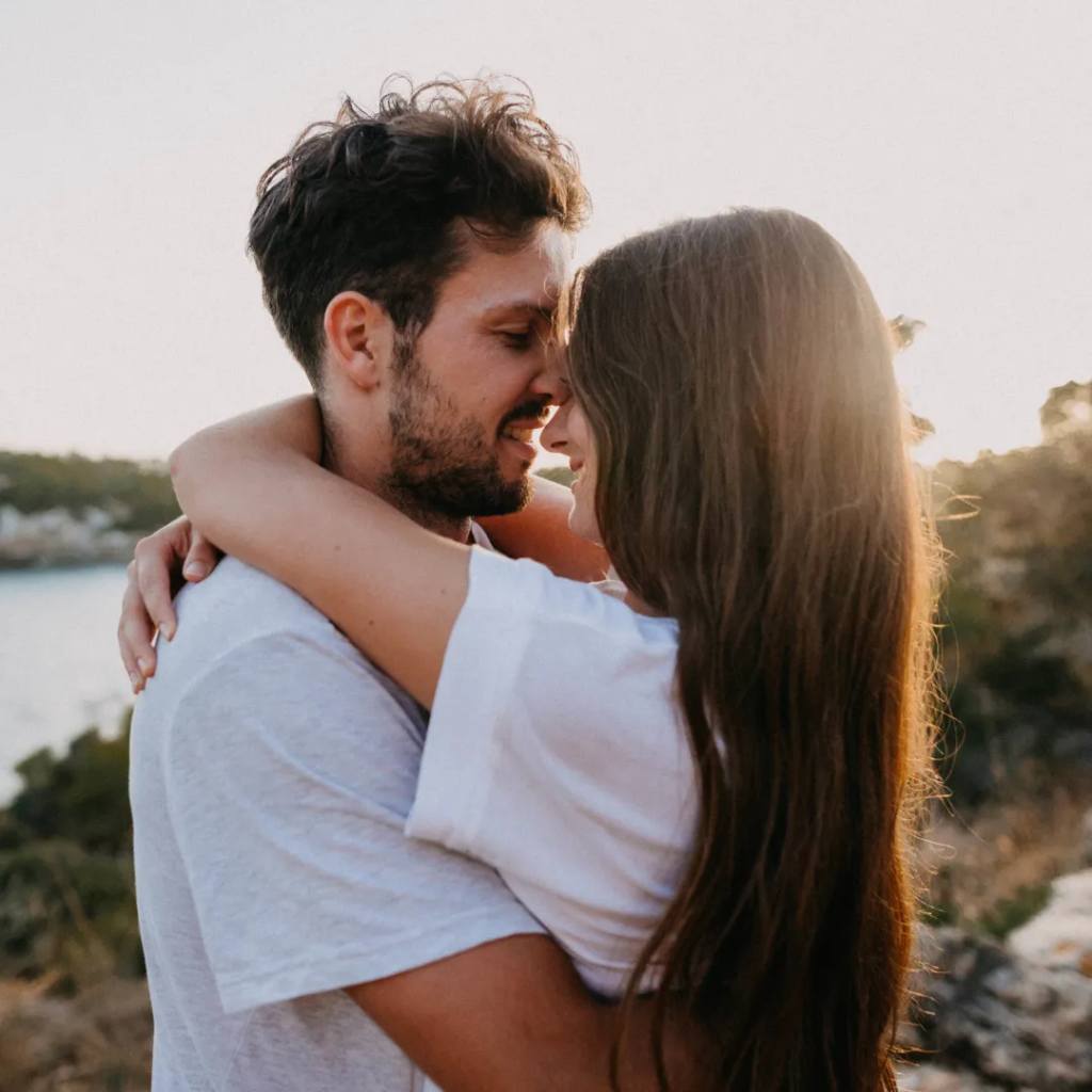 A couple embracing outdoors, seeming happy and affectionate with a scenic background.